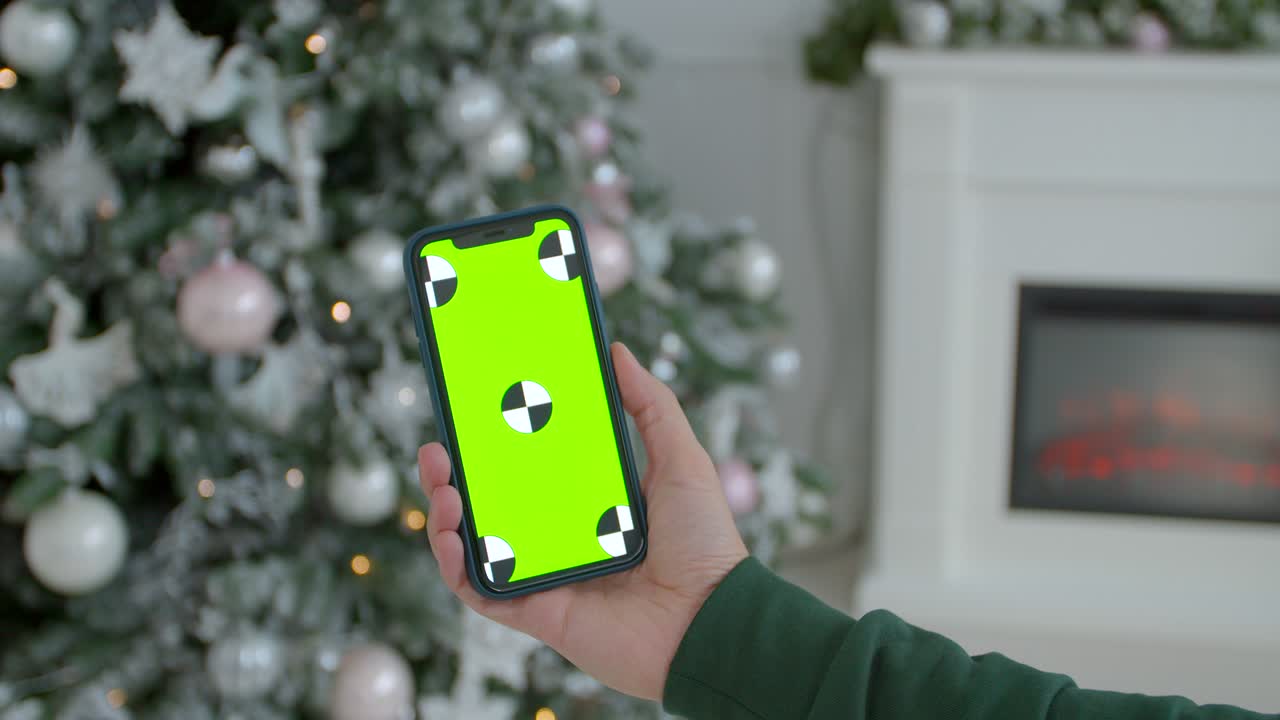 hombre sosteniendo una maqueta de teléfono inteligente pantalla verde llave de cromo en la habitación decorada para el año nuevo. primer plano de manos masculinas sosteniendo un teléfono inteligente moderno negro en las manos en el interior de la casa de navidad brillante.