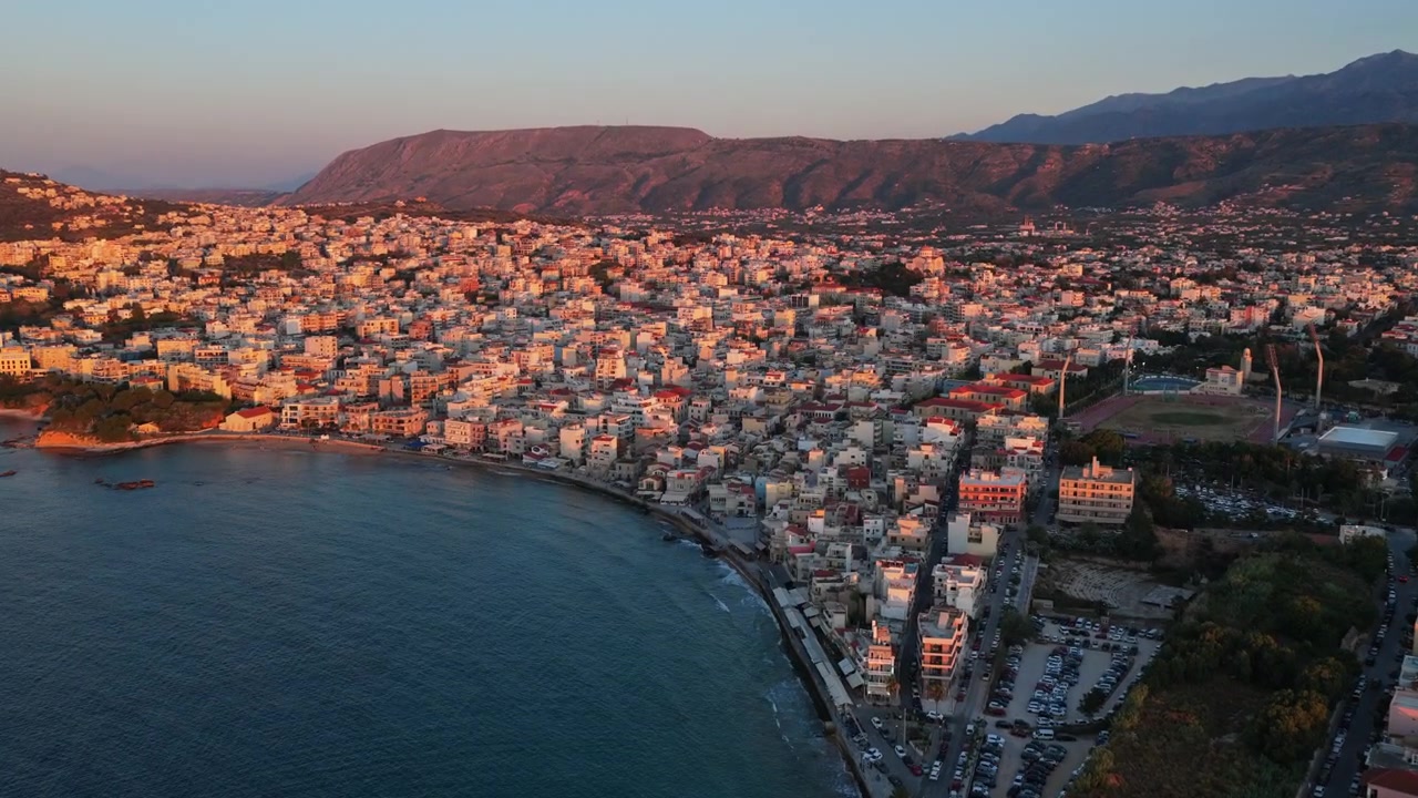 Vista aérea de drone da extensa cidade costeira com uma praia de enseada arenosa e telhados densos abaixo das montanhas