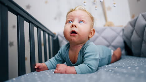 adorable blond kid lies peacefully in the cot. lovely baby portrait lying on belly in the crib. close up.