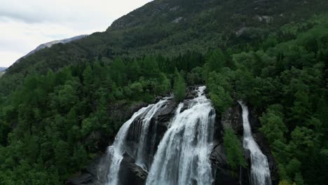 drone flies away from a waterfall and shows the untamed wilderness of norway