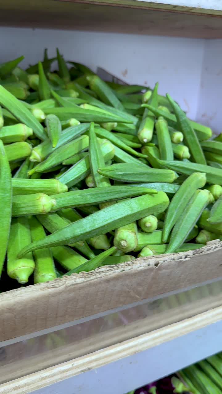 Kamera menyorot pisang, okra, dan terong berwarna cerah di bawah pencahayaan dalam ruangan yang terang di pasar.