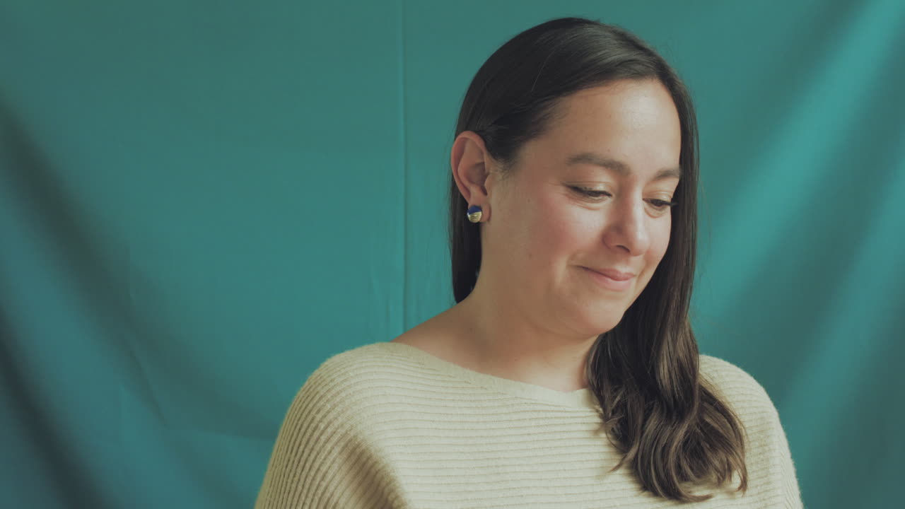 Medium shot of a young woman in focus on a professional recording set, with a solid turquoise background.