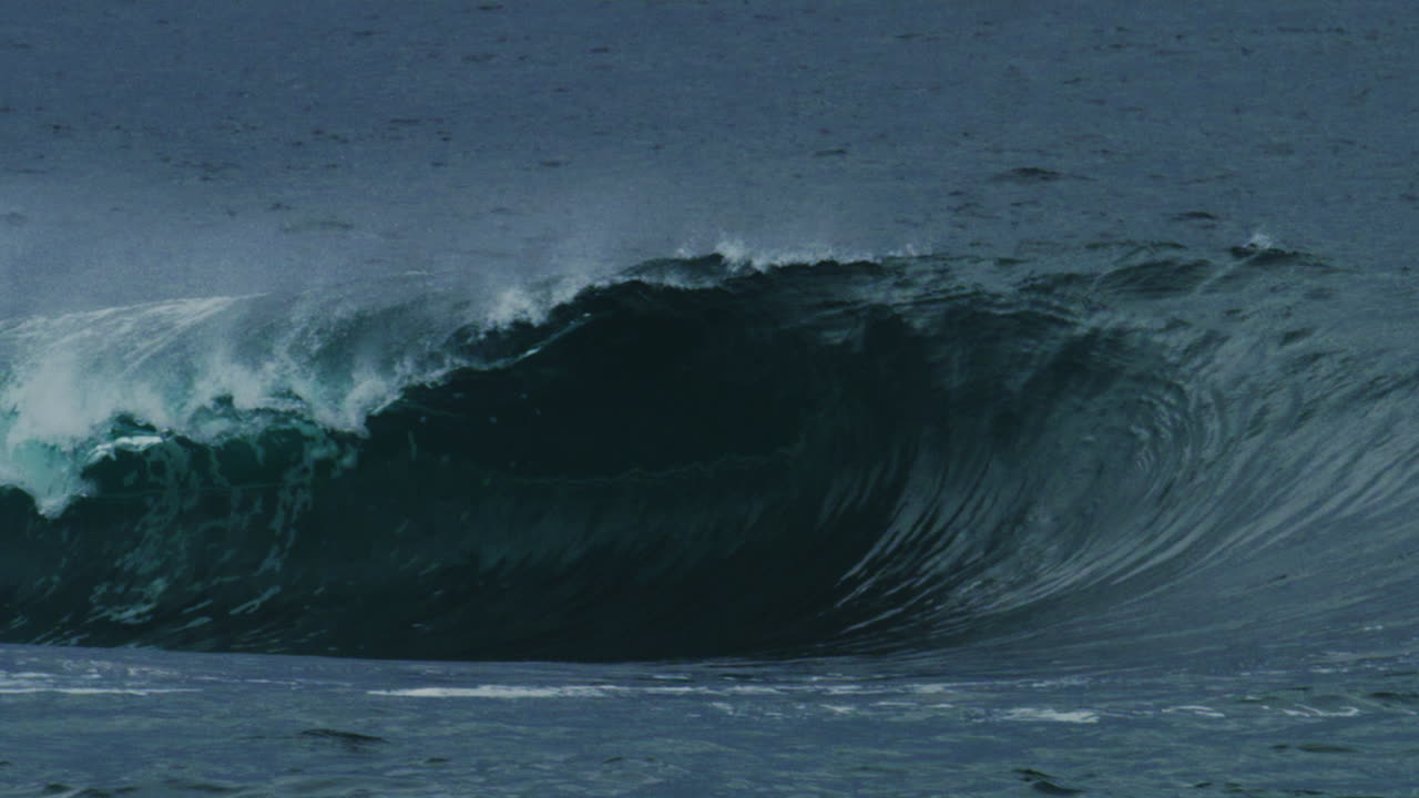 Late afternoon light cuts through wave as it crashes into powerful tube, mist rising off top