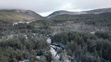 Imágenes-Cinematográficas-De-Drones-Que-Vuelan-Hacia-Un-Paisaje-Montañoso-Sobre-El-Dosel-Cubierto-De-Nieve-De-Un-Bosque-De-Pinos-Silvestres-Y-Un-Río-Congelado-Y-Helado