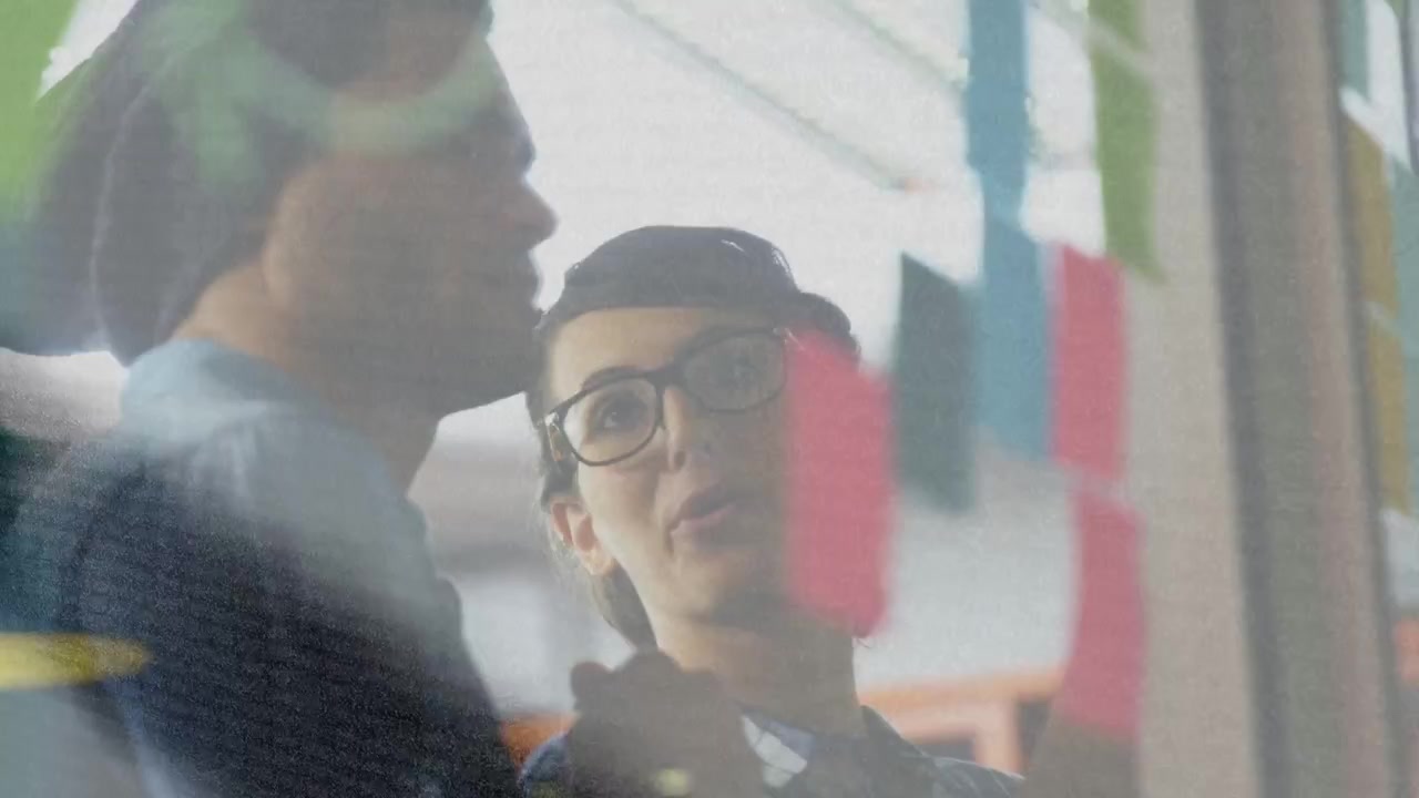 Donna che esamina post-it di vetro mentre un uomo si china e indica, avviando la pianificazione del design