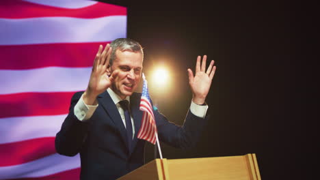 mature presidential candidate speaking with audience zoom in of friendly middle aged politician in suit gesticulating and talking with audience from podium against usa flag during election debate
