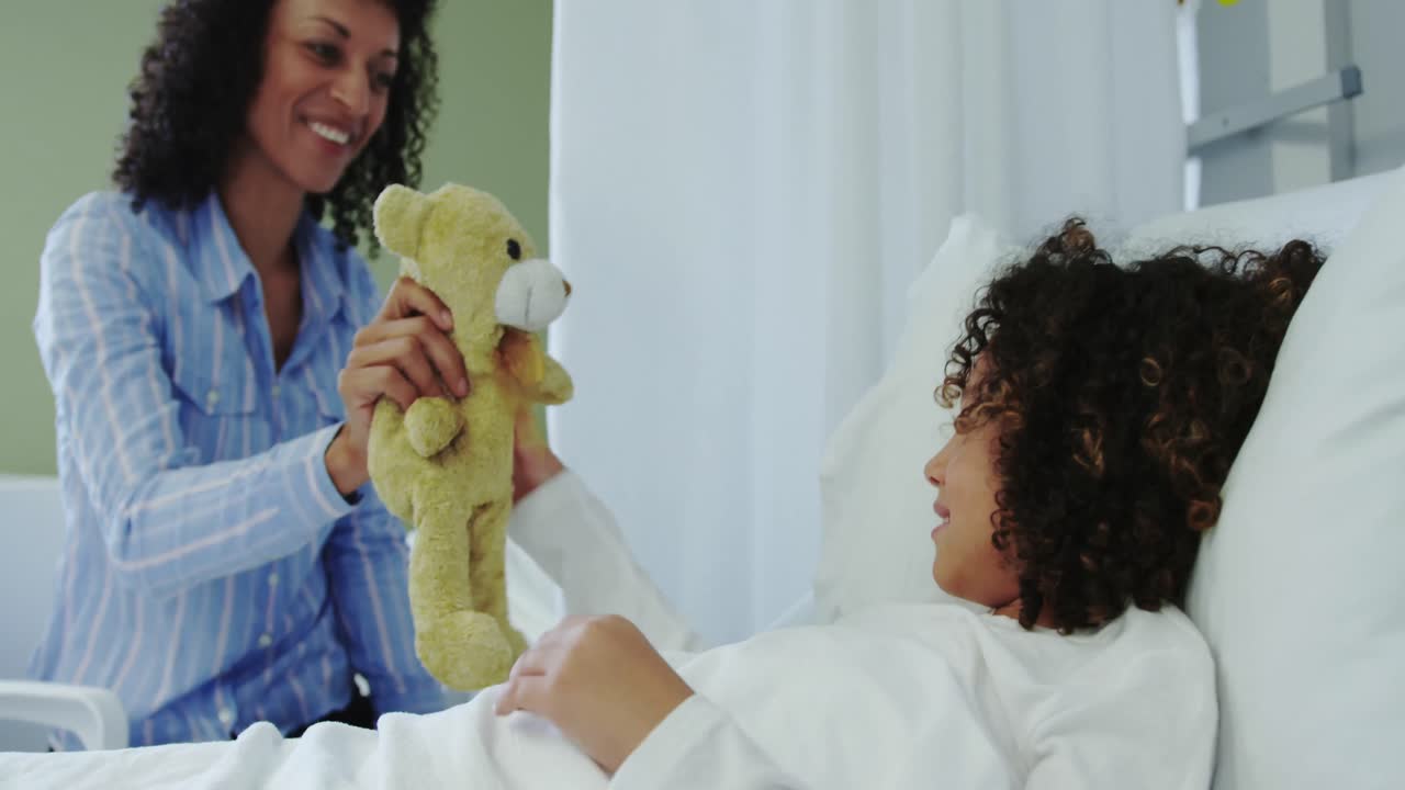 Front view of African american mother giving teddy bear to her son in the ward at hospital 4k