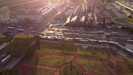 Toma-Aérea-De-Pájaros-Del-Parque-Frente-A-La-Estación-De-Tren-De-Retiro-Y-Tráfico-De-Autobuses-Para-El-Transporte-De-Pasajeros-Durante-La-Puesta-De-Sol---Ciudad-De-Buenos-Aires,-Argentina