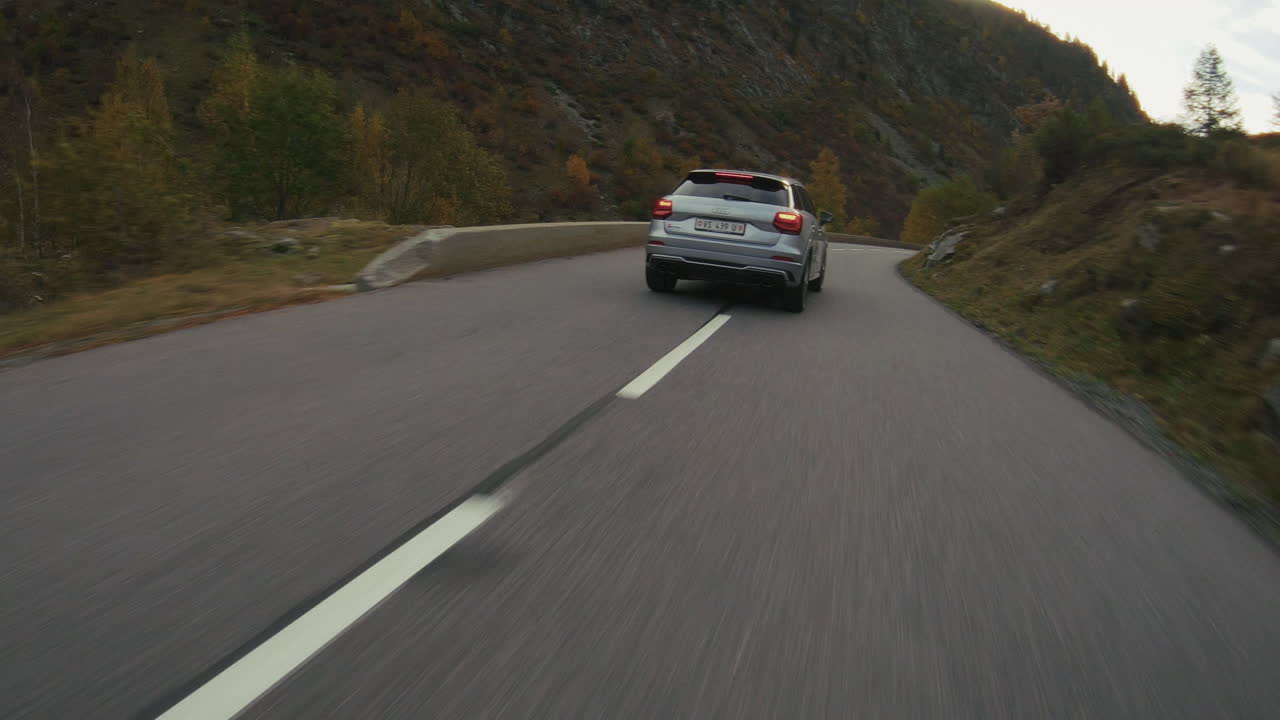 Filmato ad alta velocità realizzato con drone FPV di un'auto sportiva che percorre in modo aggressivo il passo montano del Col des Montets vicino a Chamonix durante l'autunno, con fogliame colorato, curve veloci e azione dinamica su strada alpina