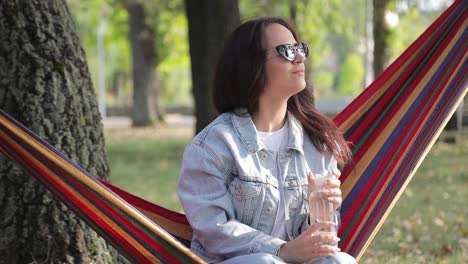 Woman relaxing in a hammock, drinking water in a park