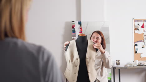 seamstress with joyful expression presents newly completed sleeveless beige blazer on black dress form to client in fashion studio, showcasing craftsmanship and fit with confident smile