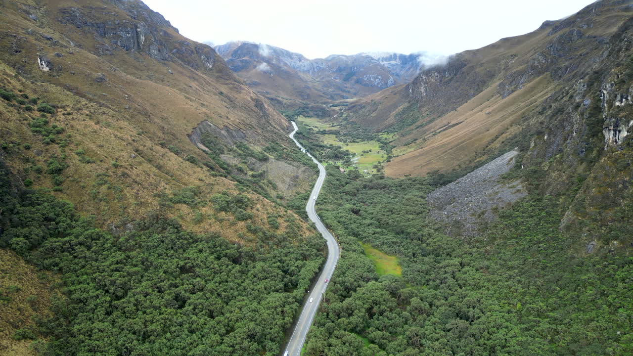 Drone footage of El Cajas mountains in Ecuador, showing a winding road cutting through lush valleys and rugged peaks, surrounded by mist and nature.