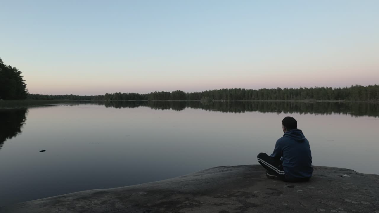 Guy walks and sits down if front of lake to watch the view