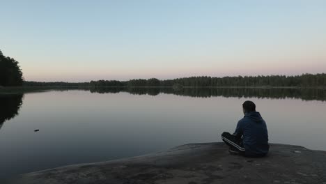 guy walks and sits down if front of lake to watch the view