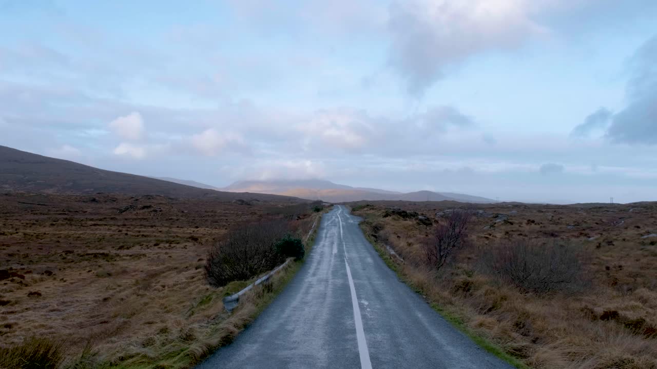 Empty Irish road leading into the horizon, surrounded by untouched nature and rolling hills