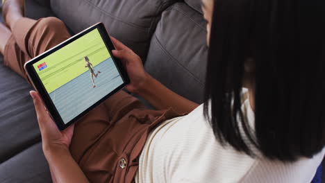 compuesto de una mujer sentada en casa en el sofá viendo atletismo corriendo evento en la tableta
