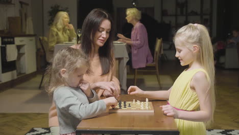 mother and her two little daughters playing chess at home 1