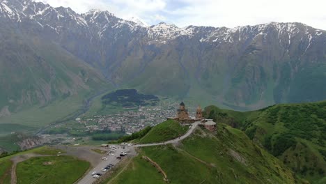 drone aerial view in georgia flying sideways gergeti trinity orthodox church in kazbegi surrounded by green mountains valley with snowed peaks