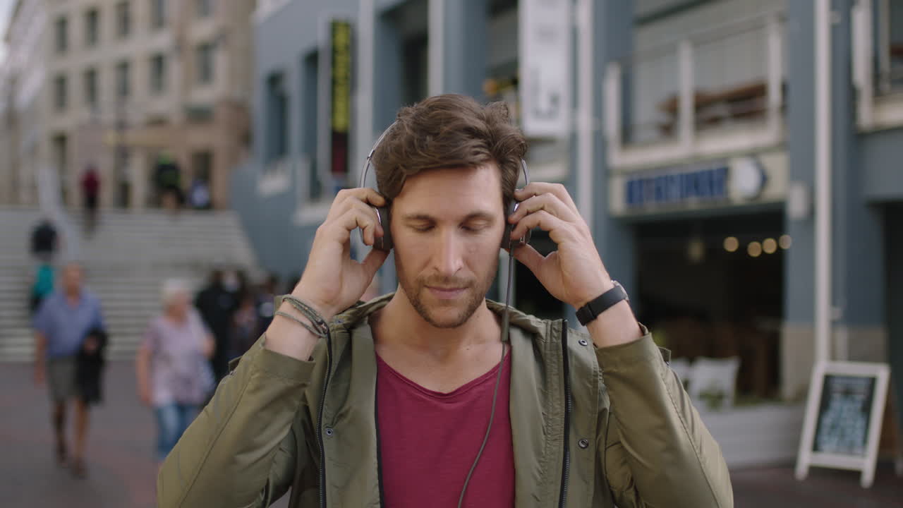 ritratto di un giovane attraente uomo caucasico in una strada urbana affollata che indossa cuffie ascoltando musica godendo dello stile di vita