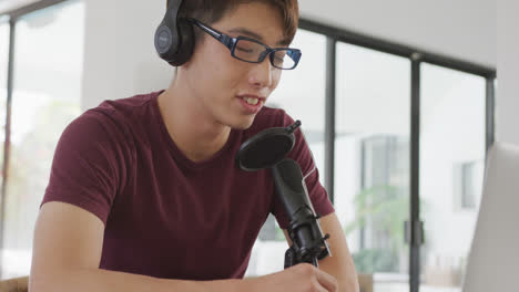 asian boy wearing headphones speaking on professional microphone to record audio podcast at home