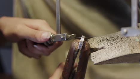 caucasian female worker shaping jewellery with saw in studio in slow motion