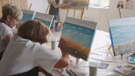 an old retired woman paints a picture together with friends. an elderly group of friends and a senior woman are drawing pictures together.