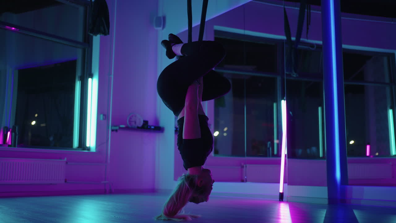 Woman hanging upside down and using yoga hammock swing while doing antigravity yoga exercise. Back view of beautiful young woman using hammock for doing pose of antigravity yoga