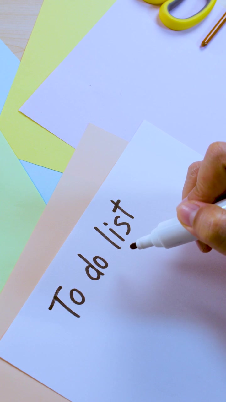 Person writes 'To do list' on white paper with marker, overhead view, natural lighting