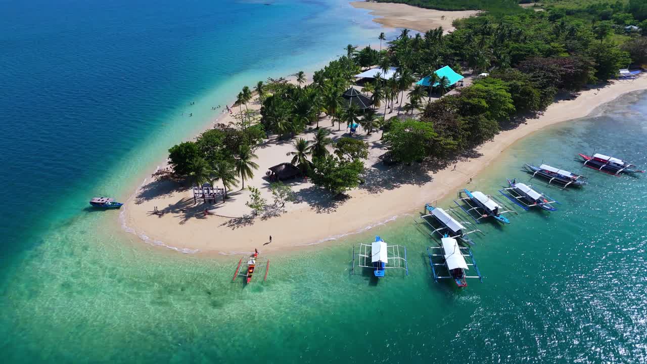 Drone aereo sopra l'isola di Cowrie nelle Filippine, isola di Palawan, che cattura le vivaci acque turchesi e la sabbia bianca incontaminata con una barca ormeggiata lungo la riva orlata di palme.