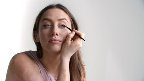 studio shot of attractive woman putting on eyeliner