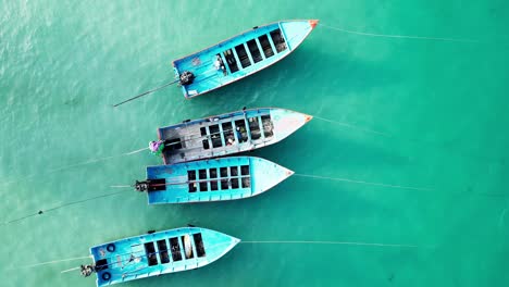 top-down aerial establishing of boats docked along the coastline of koh phangan, thailand, with turquoise waters and vibrant beach scenes