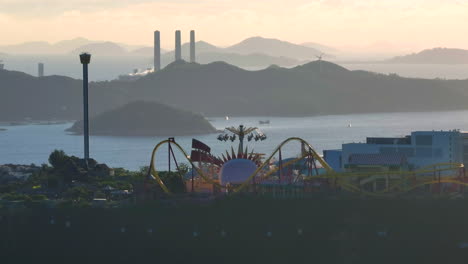 Toma-Aérea-En-órbita-Del-Parque-Oceánico-En-Hong-Kong-Y-La-Central-Eléctrica-De-La-Isla-Lamma-En-El-Fondo,-Al-Atardecer