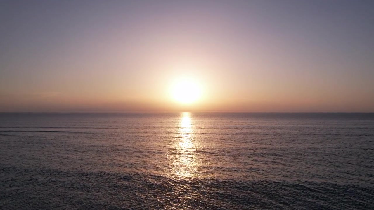 A forward drone shot moving quickly towards the ocean, with the sunset centered in the frame. The scene captures the vibrant colors of the sky during a warm summer evening.