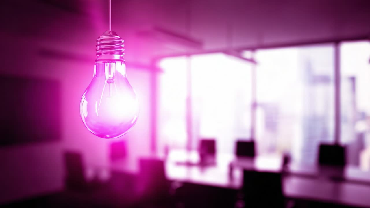 Close up of a pink light bulb hanging from the ceiling and flickering on and off, with a modern, empty office conference room blurred in the background, representing innovation and creativity