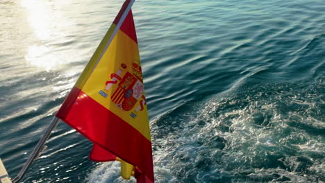 bandera española ondea en un barco mientras navega a través de las aguas azules claras cerca de málaga, capturando el espíritu marítimo bajo un sol brillante