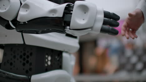 modern robotic technologies. a man communicates with a robot presses a plastic mechanical arm to the robot handshake.