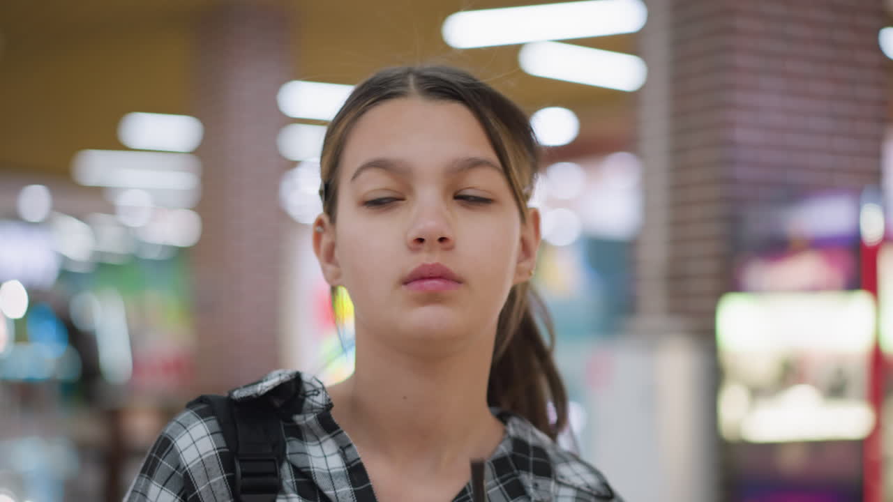 una joven elegante toma un sorbo de jugo de una taza verde mientras camina dentro de un centro comercial, se vuelve lentamente, rodeada de una atmósfera vibrante y moderna con luces brillantes borrosas en el fondo