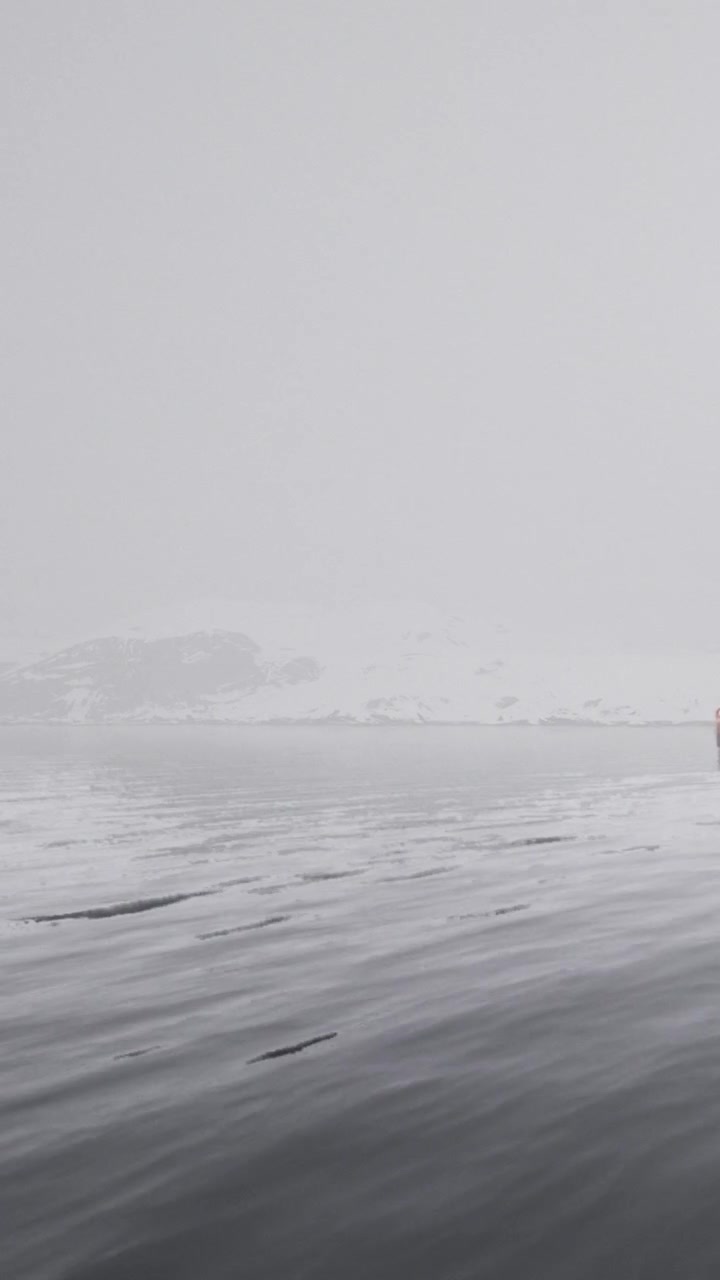 Snowy landscape with water and distant hills on a cloudy day