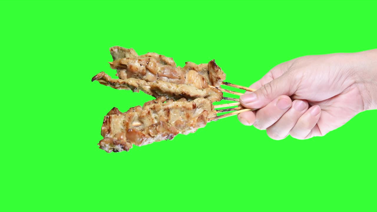 초록색 스크린 배경에 바베큐 사타이 을 들고 있는 손.