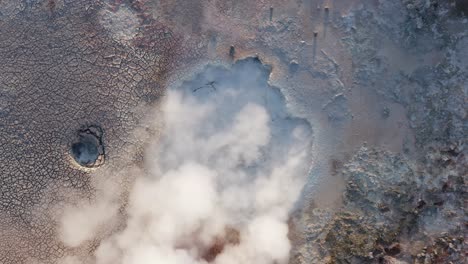 Top-down-aerial-at-boiling-mud-pool-creating-toxic-gas,-cracked-surface