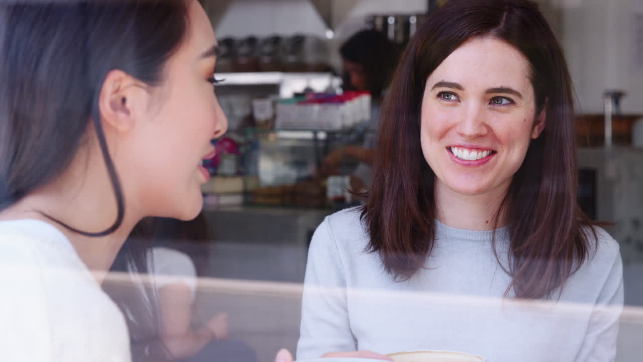 amigas riendo en una cafetería, vistas a través de la ventana.