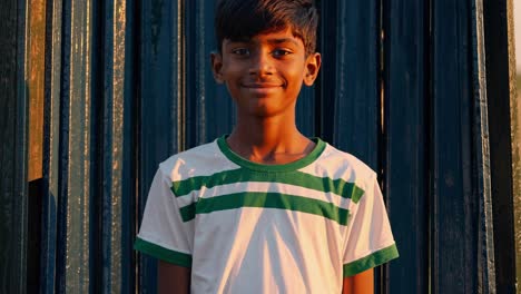 young boy smiles warmly while standing against a rustic background, captured during a beautiful summer sunset, reflecting the joy and innocence of youth