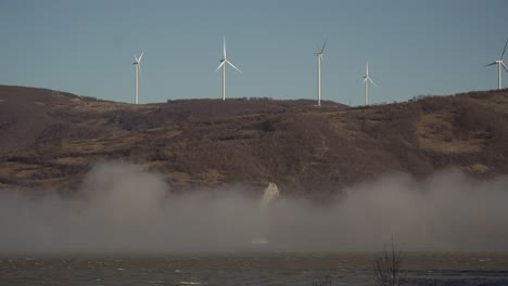 molinos de viento en la colina detrás del río en la niebla