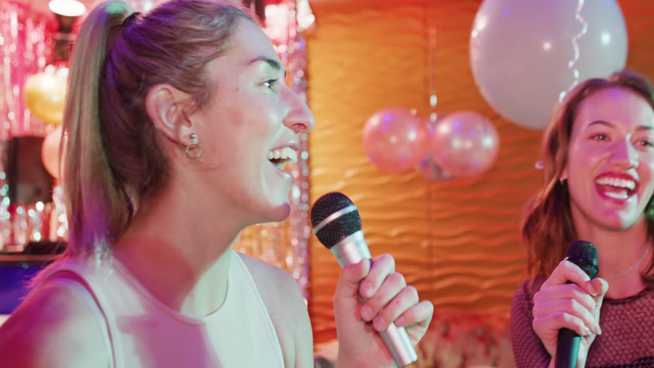 Video of two happy caucasian female friends singing karaoke at a nightclub bar