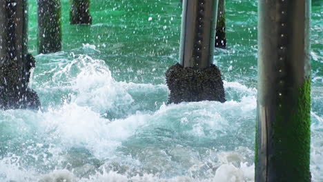 waves crashing against pilings in slow motion under a pier at new port beach in california