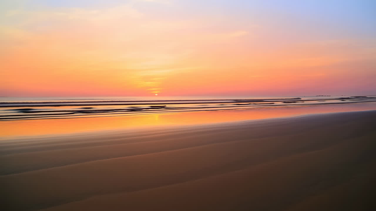Spokojne fale oceanu na piaszczystej plaży o zachodzie słońca