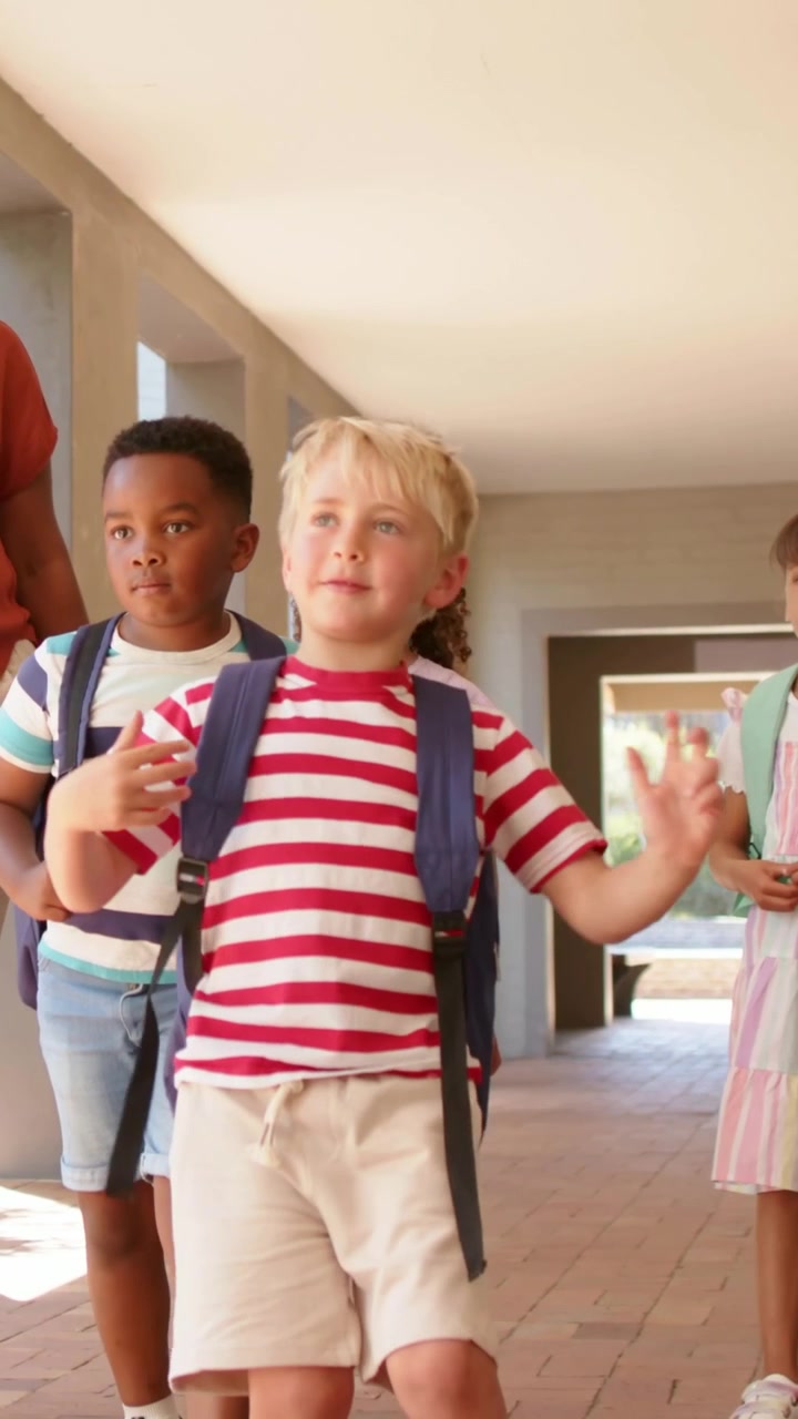 Lead boy walking path with backpack, sunlit schoolyard ahead causing playful moves, teacher walking