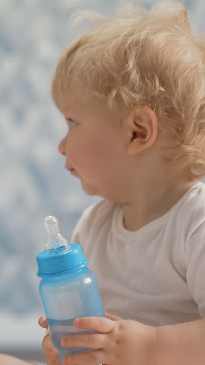 cute little child with bottle of water sits near elder sister playing with modern smartphone in light spacious room of contemporary flat staying home