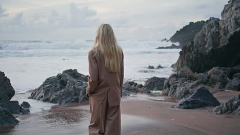 mujer pacífica admirando el océano caminando playa de arena. vista trasera modelo elegante yendo