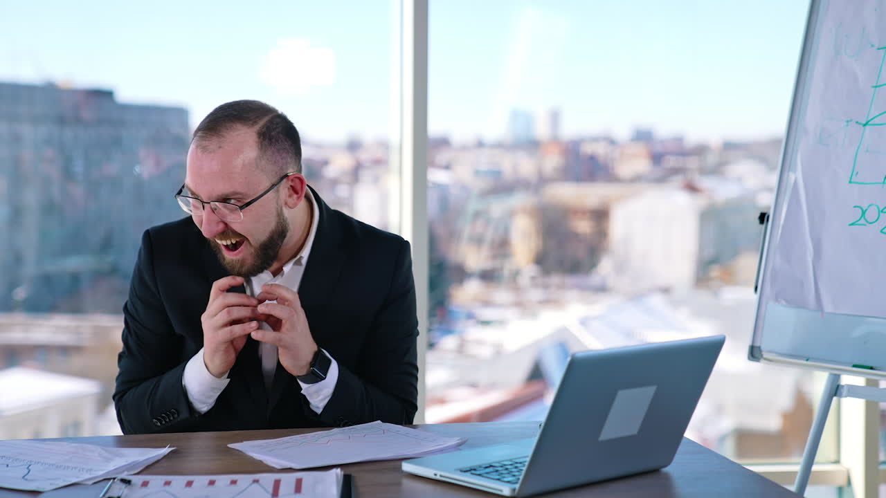 Funny businessman. Insane man in suit sitting at the table in office centre and doing mad things with his arms and fingers.